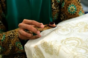 Close-up of a hand creating intricate batik patterns using a traditional wax pen.