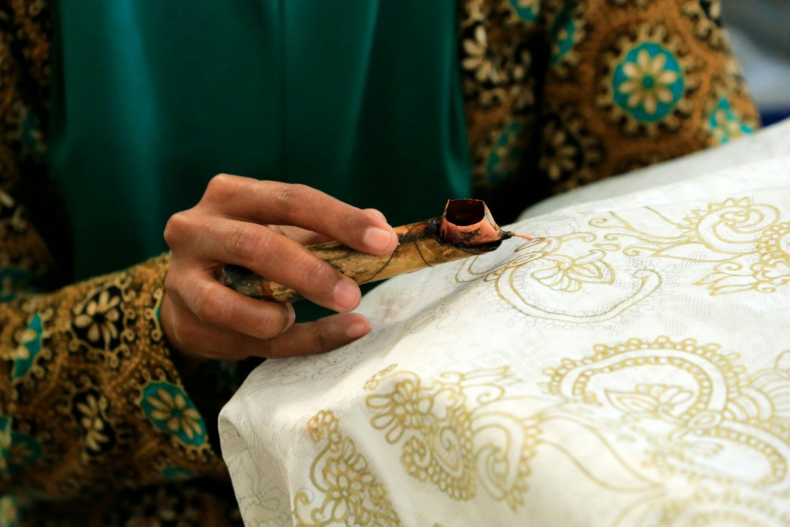 Close-up of a hand creating intricate batik patterns using a traditional wax pen.