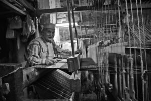 Black and white photo of a traditional weaver working at a loom in Fes, Morocco.